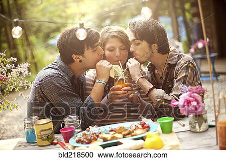Stock Image - Friends sharing soda at picnic table in forest. Fotosearch