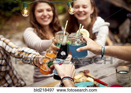 Stock Photo - Friends toasting with soda at picnic table. Fotosearch