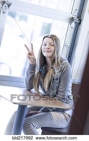 Stock Image - Girl giving peace sign at table. Fotosearch