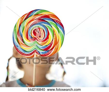 Stock Image - Girl holding lollipop in front of face. Fotosearch