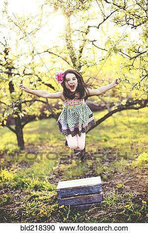 Stock Image - Girl jumping for joy in orchard. Fotosearch