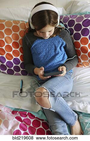 Stock Photo - Girl listening to headphones with digital tablet on bed. Fotosearch