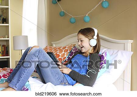 Girl listening to headphones with digital tablet on bed View Large Photo Image Stock Photograph - Girl listening to headphones with digital tablet on bed. Fotosearch