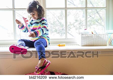 Stock Photo - Girl playing with toys in windowsill. Fotosearch