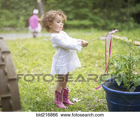 Stock Photograph - Girl playing with wand in backyard garden. Fotosearch