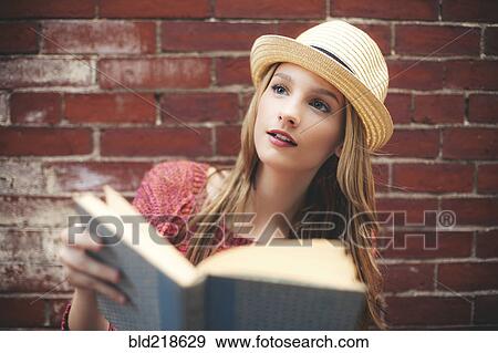 Stock Photo - Girl reading book near brick wall. Fotosearch