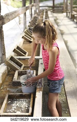 Stock Photo - Girl shoveling rocks in bucket in trough. Fotosearch