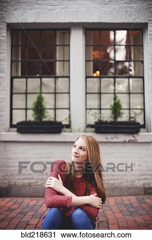 Stock Image - Girl sitting on brick sidewalk. Fotosearch