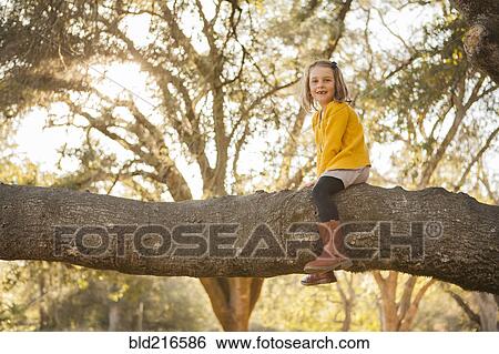 Stock Photograph - Girl sitting on tree branch in park. Fotosearch