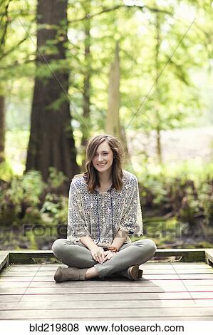 Stock Photo - Girl sitting on wooden patio near tree. Fotosearch