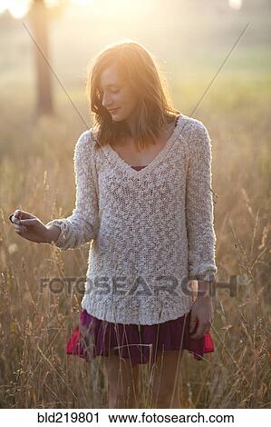 Stock Image - Girl standing in tall grass in rural field. Fotosearch