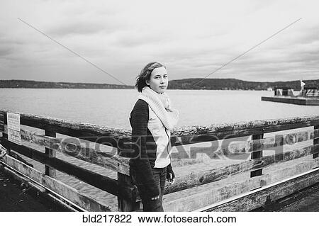 Stock Image - Girl standing on wooden dock at lake. Fotosearch