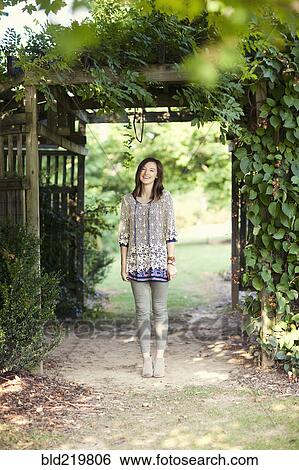 Stock Photograph - Girl standing under archway in garden. Fotosearch