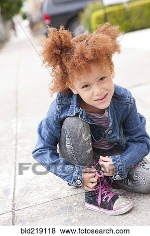 Stock Photo - Girl tying sneaker shoelaces on sidewalk. Fotosearch
