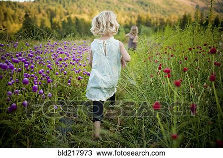 Stock Image - Girl walking in rural field of flowers. Fotosearch