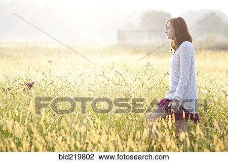 Stock Image - Girl walking in tall grass in rural field. Fotosearch