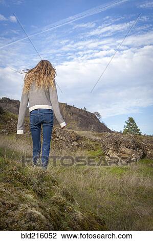 Stock Image - Girl walking on grassy hillside. Fotosearch