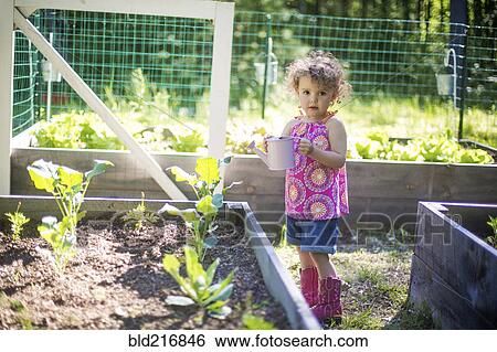 Stock Photograph - Girl watering plants in garden. Fotosearch