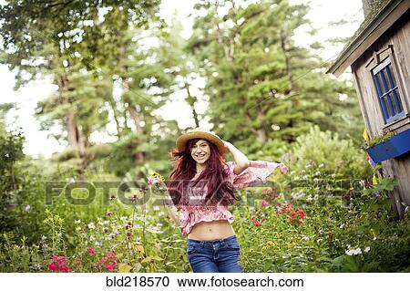 Stock Image - Girl wearing straw hat running in garden. Fotosearch