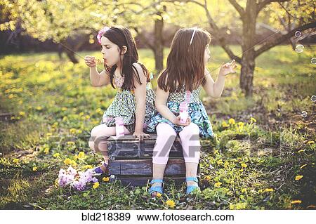 Stock Photo - Girls blowing bubbles in orchard field. Fotosearch