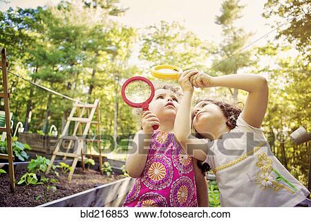 Stock Image - Girls examining caterpillar with magnifying glass. Fotosearch