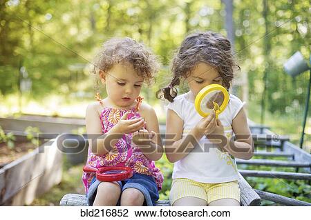 Stock Image - Girls examining garden plants with magnifying glass. Fotosearch