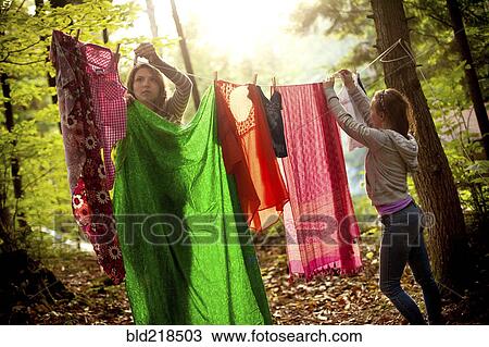 Girls hanging laundry on clothesline in forest View Large Photo Image Stock Image - Girls hanging laundry on clothesline in forest. Fotosearch