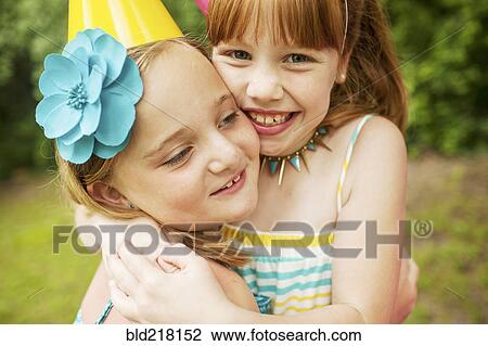 Stock Image - Girls hugging at birthday party outdoors. Fotosearch
