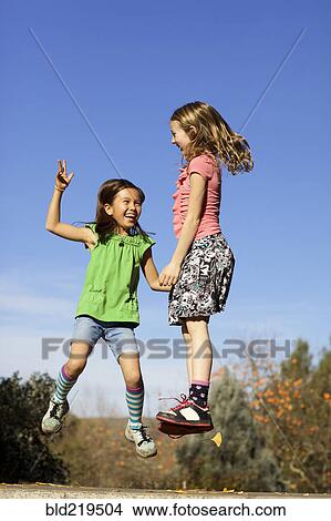 Picture - Girls jumping for joy on stone wall. Fotosearch