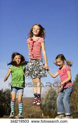 Stock Image - Girls jumping for joy on wall. Fotosearch