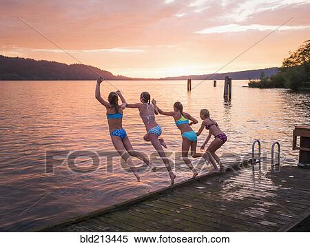 Stock Photography - Girls jumping into lake from wooden dock. Fotosearch