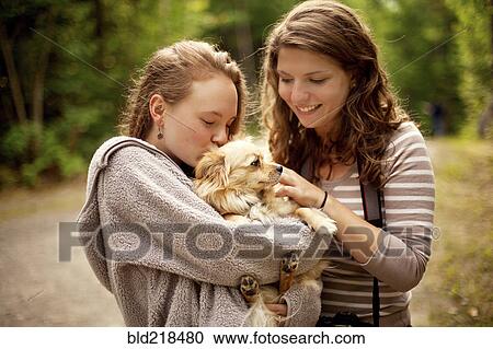 Stock Image - Girls petting puppy in forest. Fotosearch