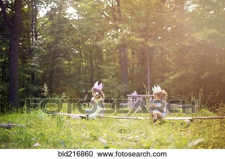 Stock Image - Girls playing telephone on wooden log in garden. Fotosearch