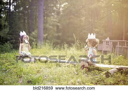 Stock Photo - Girls playing telephone on wooden log in garden. Fotosearch