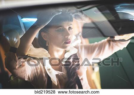 Stock Photo - Glamorous mixed race woman checking hair in car mirror. Fotosearch
