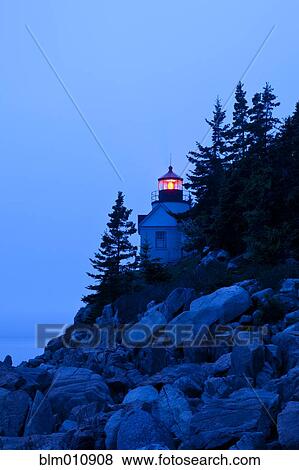 Stock Photo - Glowing lighthouse on rocky shore. Fotosearch