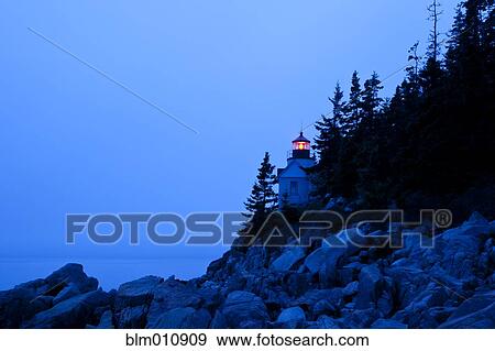 Stock Photo - Glowing lighthouse on rocky shore. Fotosearch