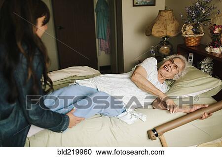 Stock Image - Granddaughter helping grandmother into bed. Fotosearch