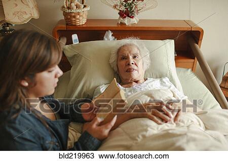Stock Image - Granddaughter reading to grandmother in bed. Fotosearch