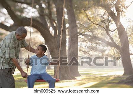 Stock Photography - Grandfather pushing grandson on swing. Fotosearch