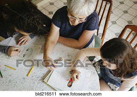 Stock Image - Grandmother and grandchildren drawing at table. Fotosearch
