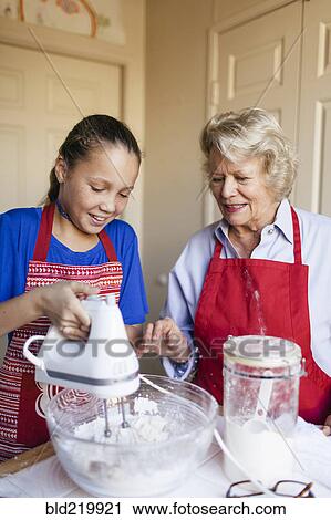Stock Image - Grandmother and granddaughter baking in kitchen. Fotosearch