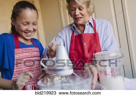 Stock Image - Grandmother and granddaughter baking in kitchen. Fotosearch