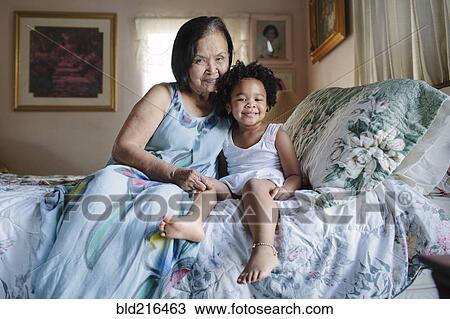 Stock Image - Grandmother and granddaughter hugging on bed. Fotosearch