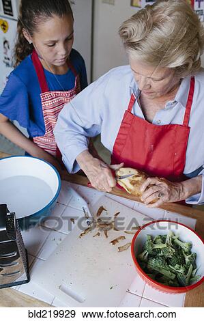 Stock Photo - Grandmother and granddaughter peeling potato in kitchen. Fotosearch