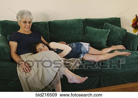 Grandmother and granddaughter sitting on sofa in living room View Large Photo Image Stock Photo - Grandmother and granddaughter sitting on sofa in living room. Fotosearch