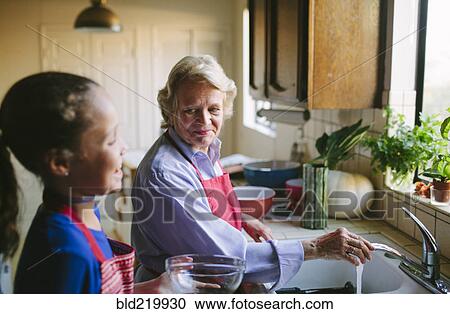 Stock Image - Grandmother and granddaughter washing bowl in kitchen sink. Fotosearch