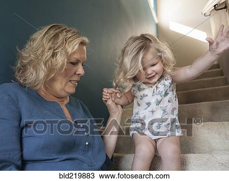 Stock Image - Grandmother helping granddaughter walking on staircase. Fotosearch