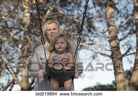 Picture - Grandmother pushing granddaughter on swing at playground. Fotosearch