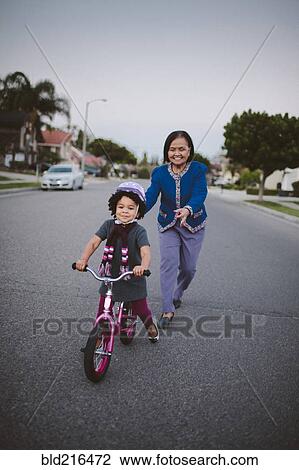 Grandmother teaching granddaughter to ride bicycle on suburban street View Large Photo Image Stock Image - Grandmother teaching granddaughter to ride bicycle on suburban street. Fotosearch